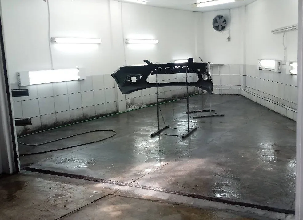 Parachoque suspenso em suporte dentro da cabine de pintura da oficina