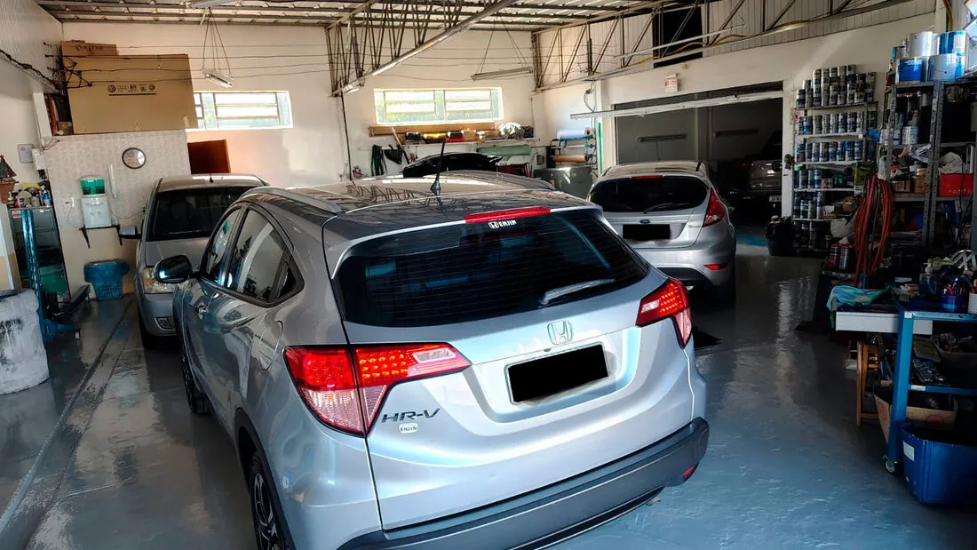 Carros em atendimento dentro da oficina, com estoque de tintas ao fundo
